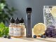 Close-up lifestyle photo of vape device and wellness e-liquid bottles on a wooden surface with mint, lavender, lemon, and blueberries in soft natural light.